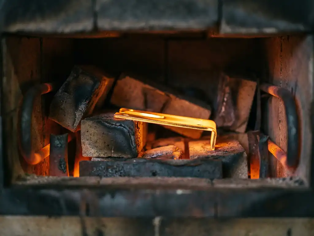 Goldbeschichtetes Metallbauteil glüht orange-amber in einem Industriehochofen, Nahaufnahme mit Wärmeflimmern und dunkler Ofenkammer.