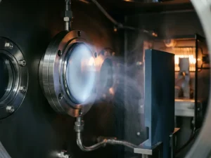 Platin-Sputtertarget in einer Vakuumkammer mit kondensierenden Dampfpartikeln auf dunklem Substrat, bläulich-weißes Industrielicht.