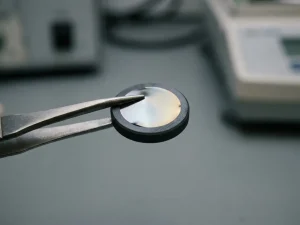 Irisierender Platinfilm wird mit Metallpinzette auf poliertes dunkles Keramiksubstrat aufgetragen, Makroaufnahme mit Silber- und Goldreflexen.