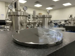 Platinfarbene Metallscheibe mit PVD-Beschichtung auf einer Seite und feinen ALD-Dampfschwaden auf der anderen, Laborumgebung.